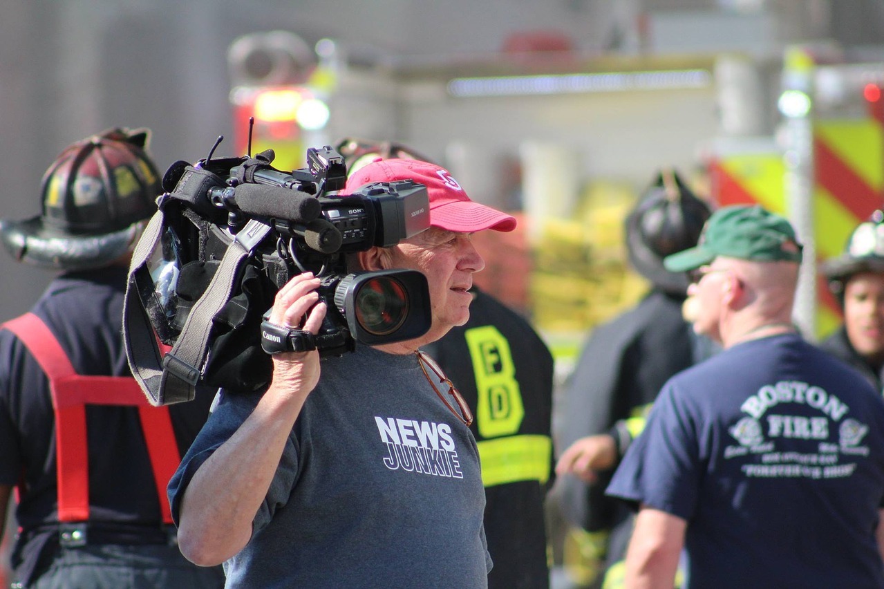 Man with video camera with firemen behind him