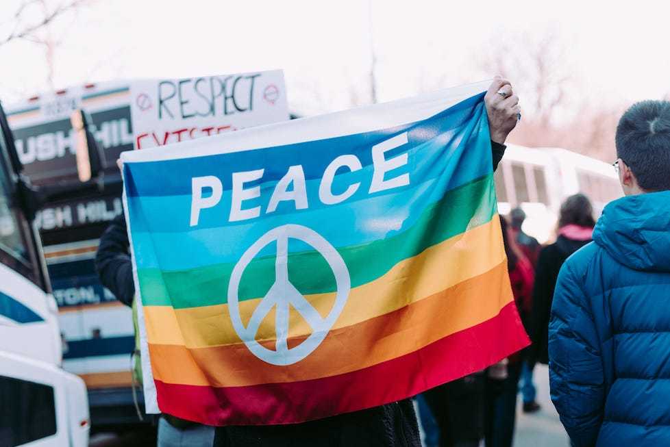 Protesters at a march holding up a rainbow flag with a peace sign on it.