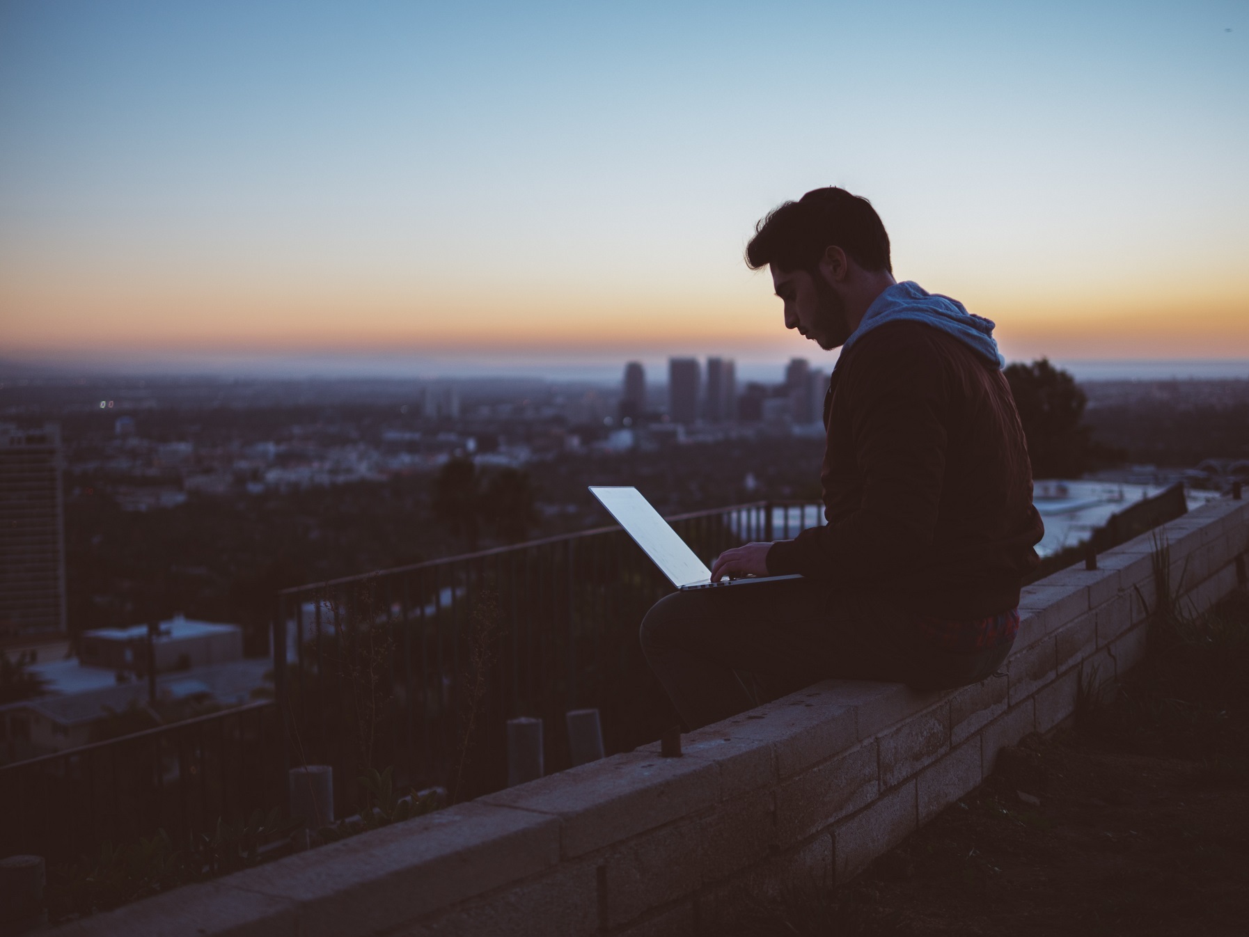 man on rooftop at sunset typing on computer