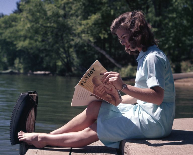 Woman reading Playboy by a lake