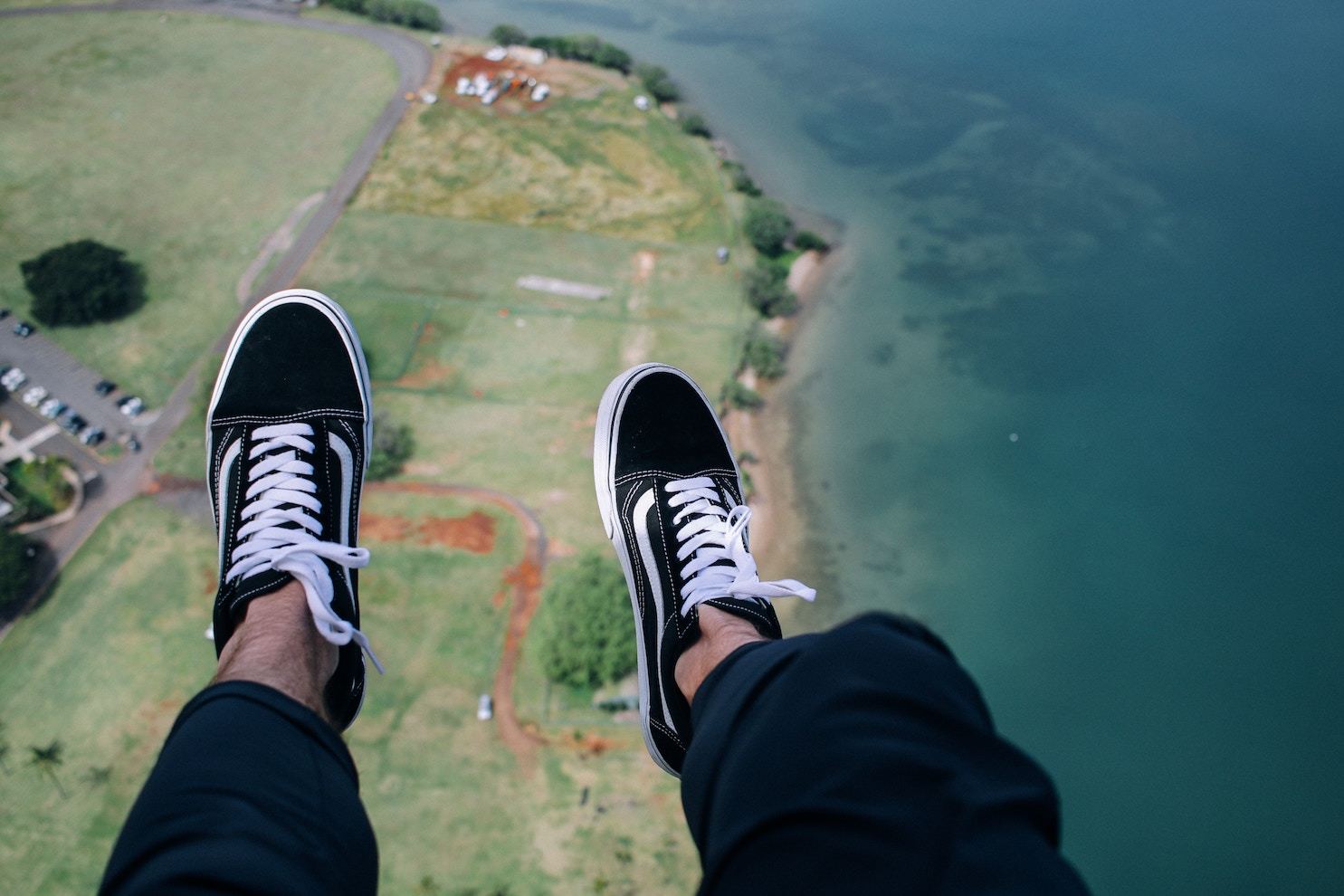 A man's legs, in baggy pants and sneakers, hang above the shoreline as seen from above