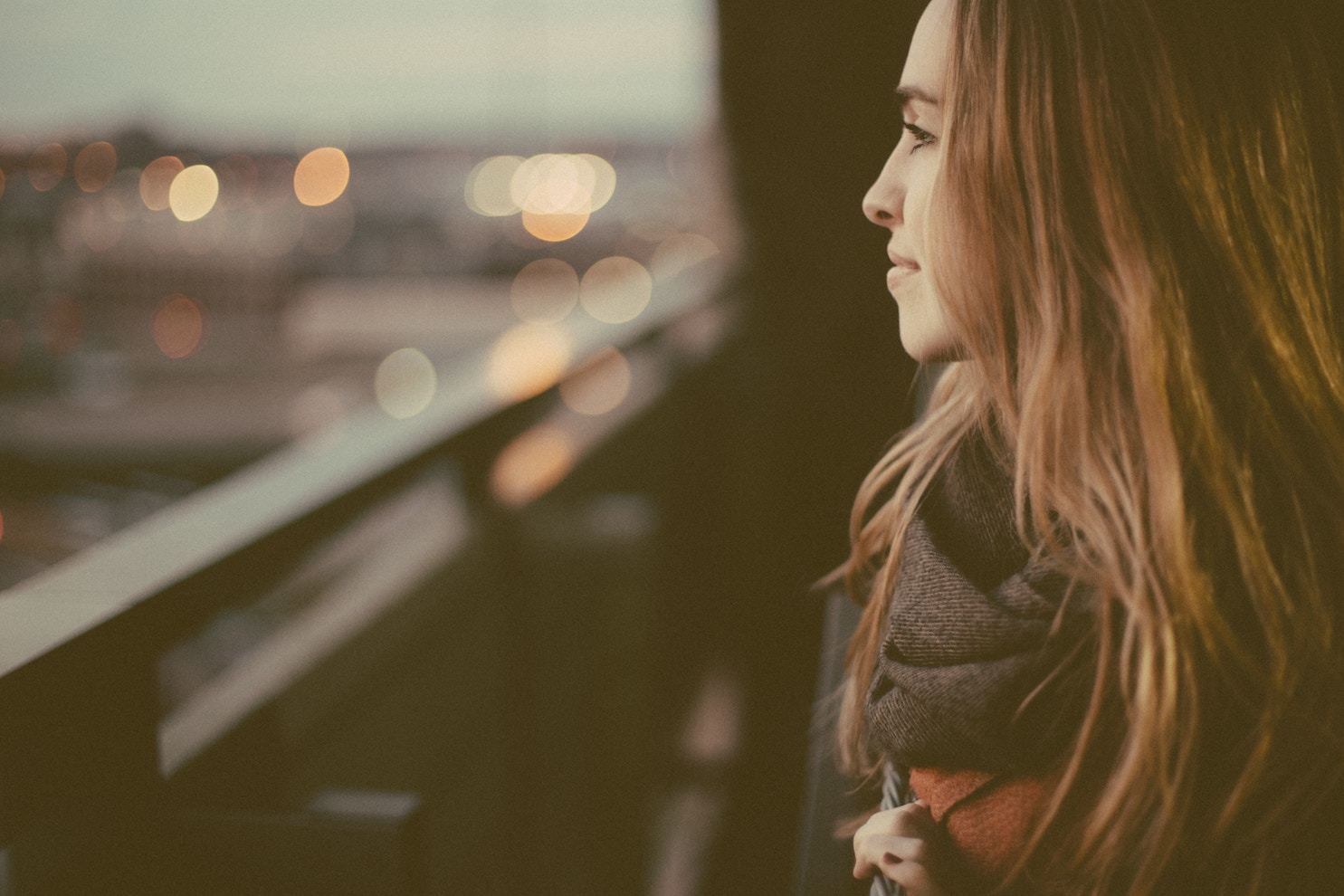 a woman, seen in profile, looks out the window over a blurry city