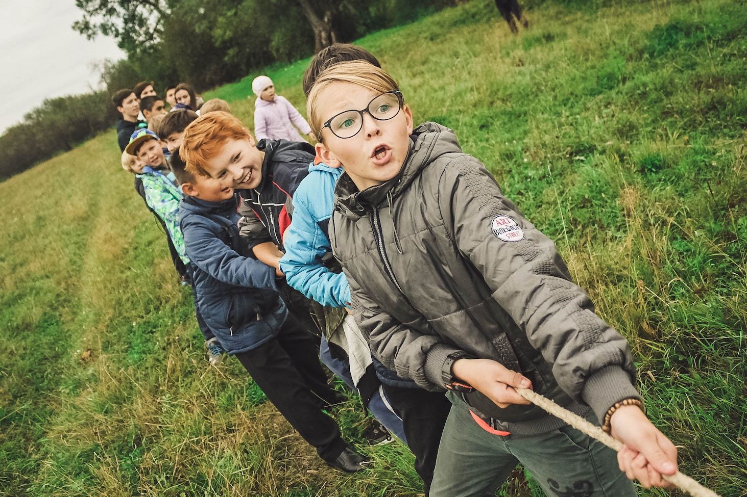 children play tug-of-war in a grassy field