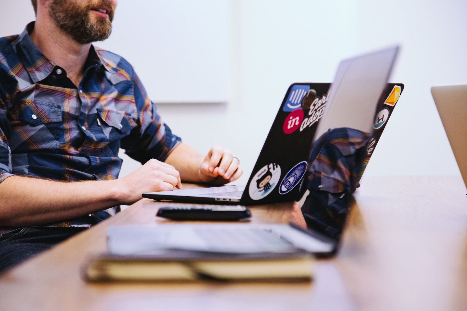 A bearded man in a flannel shirt with a sticker-covered laptop