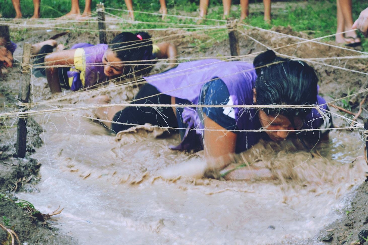 Women crawl through a muddy obstacle course