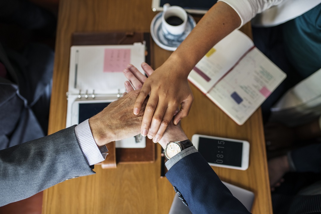 Team members put their hands in together over a conference room table.