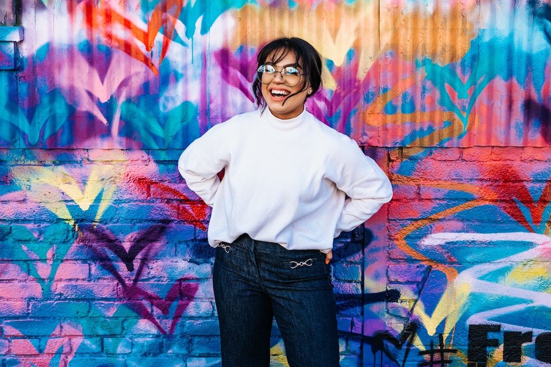 smiling woman in front of rainbow wall (Unsplash)