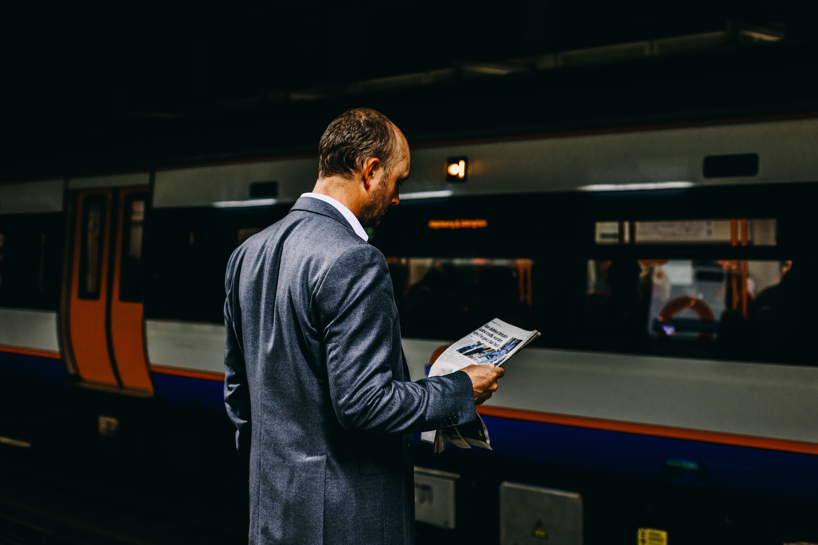 Man standing on train platform reading newspaper