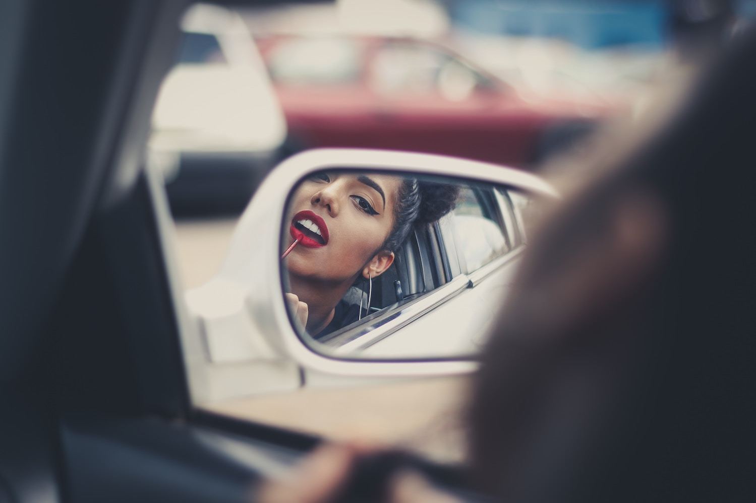 woman applies lipstick in car mirror