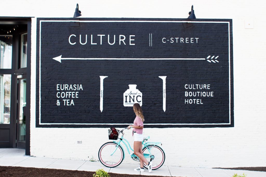 Woman riding a bike in front of a billboard reading "Culture"