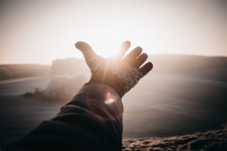 A man holds his hand out at the sight of a sunset.
