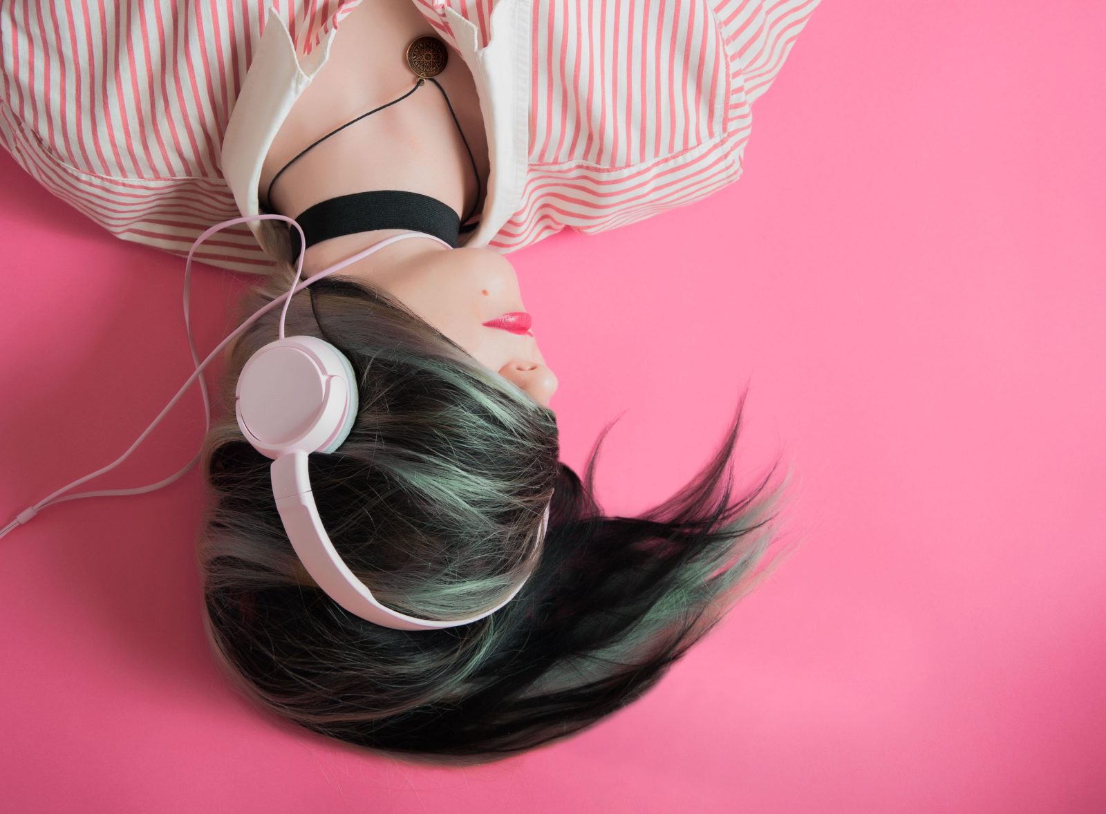 A woman listens to a podcast wearing big headphones while laying on a fluorescent pink floor.