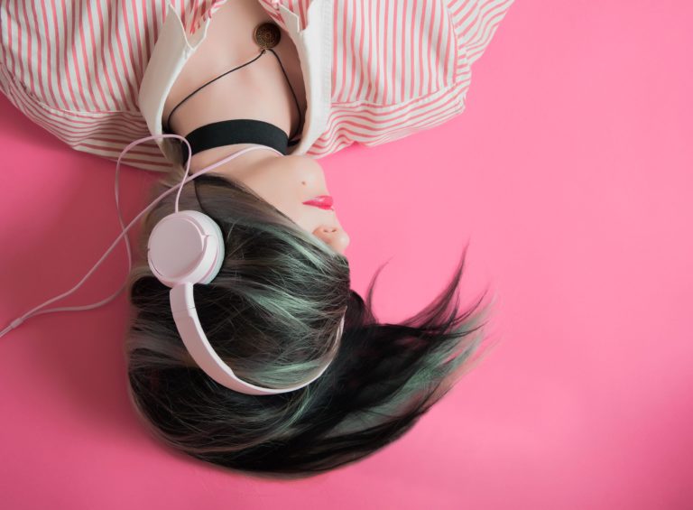 A woman listens to a podcast wearing big headphones while laying on a fluorescent pink floor.