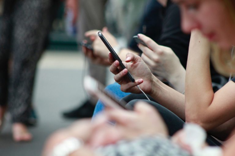 A line of people look closely at their cell phones.
