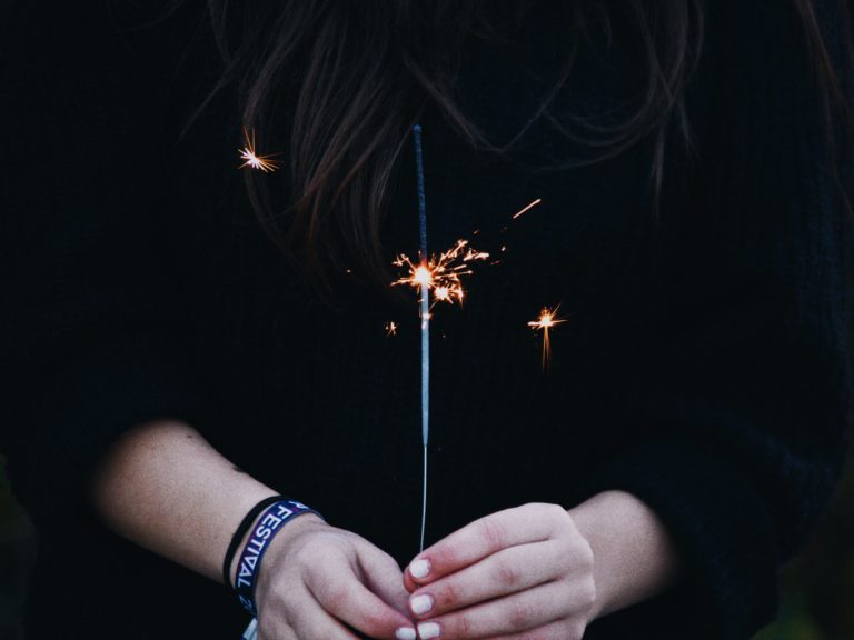 A woman with white painted nails holds a sparkler during a New Year's celebration.