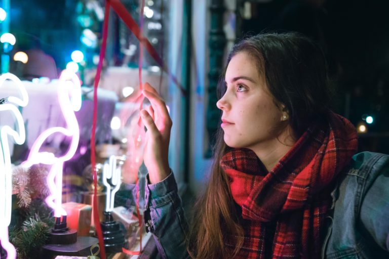 A woman with brown hair wearing a plaid scarf looks into a holiday window display.