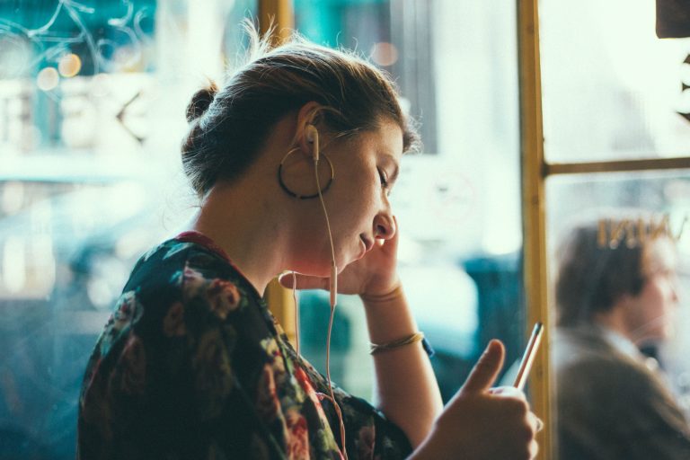 A woman in a cafe listens to a B2B podcast through earbuds