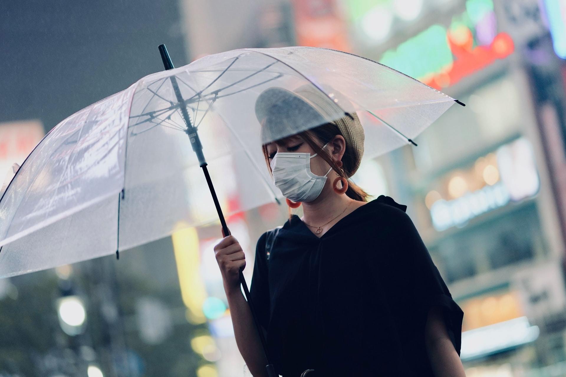 Woman in mask walks with umbrella during coronavirus