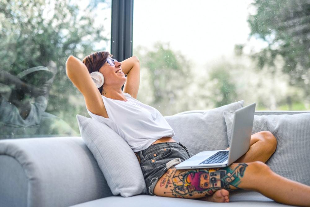 A woman wearing over-ear headphones smiles and takes a break from creating a marketing resilience plan on her laptop.