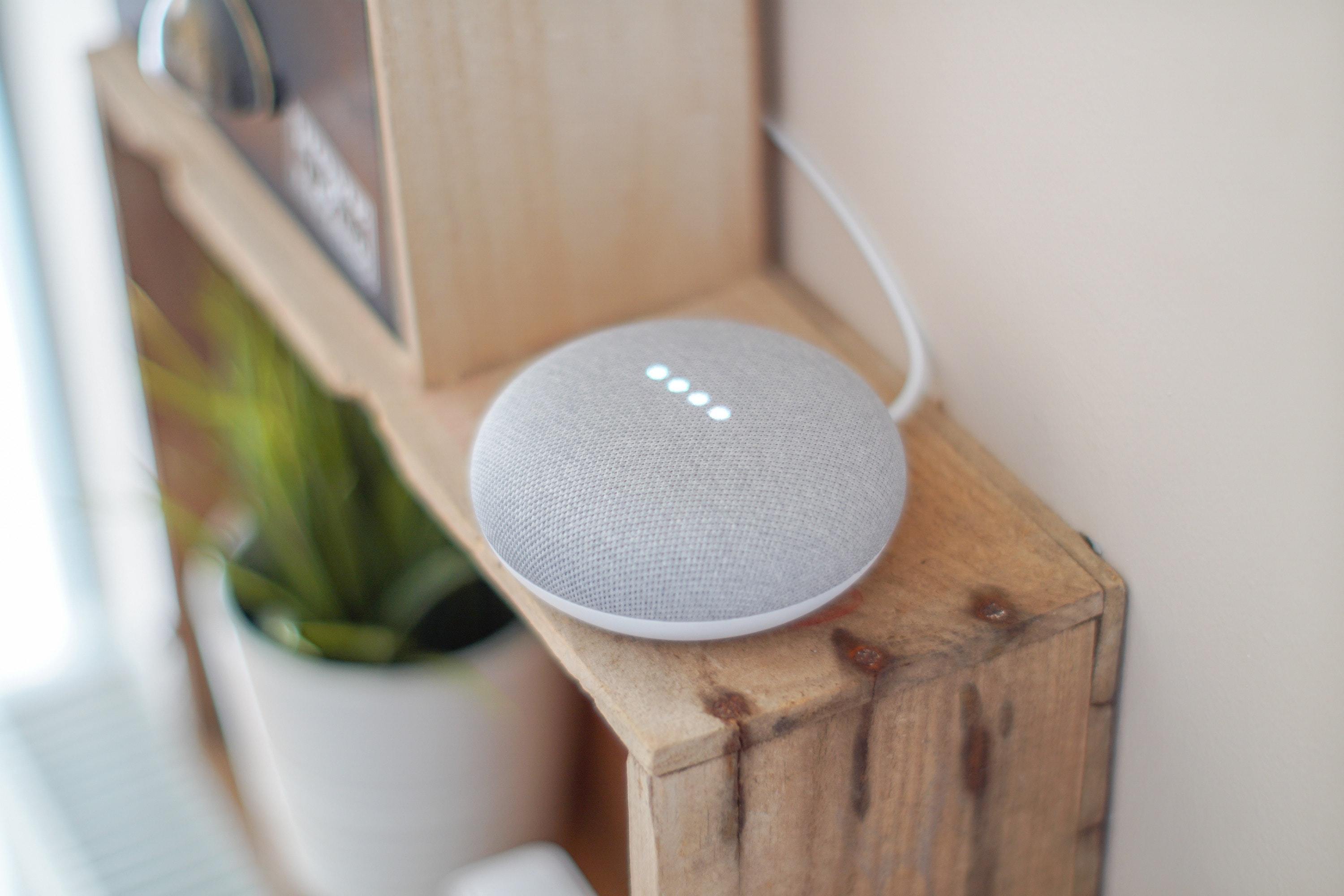 A grey smart speaker on a wood shelf
