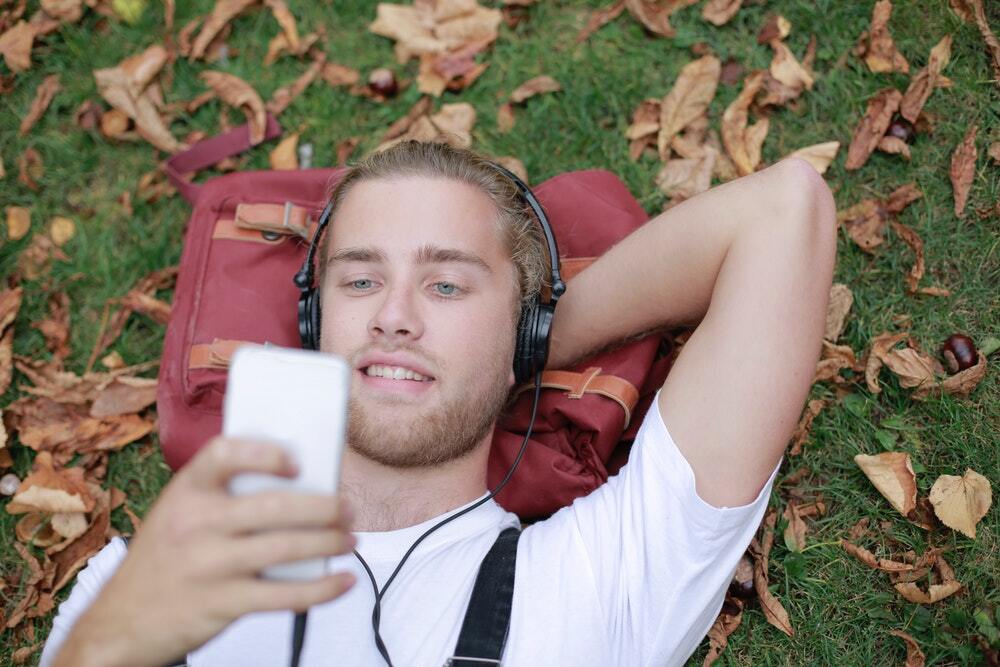 Man lying on grass listening to a podcast and reading its transcript.