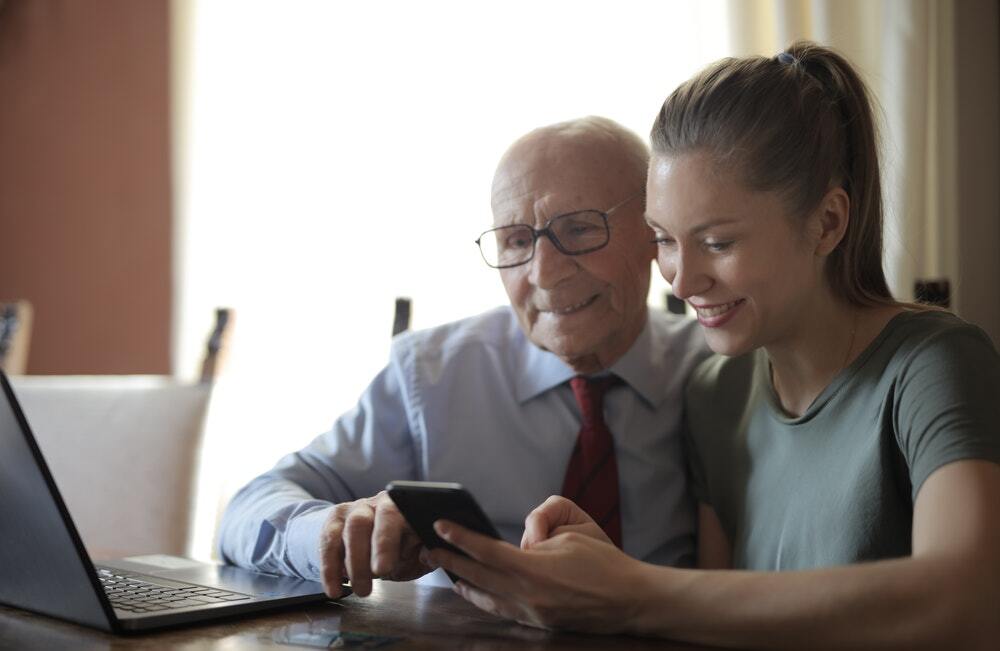 A positive elderly man and a smiling young woman watching a quality content marketing video.