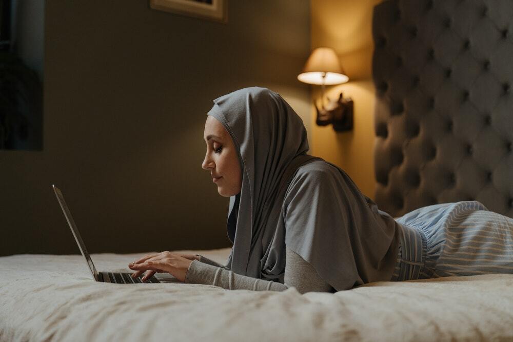 A woman in a hijab sitting on a bed watching a live content marketing webinar.
