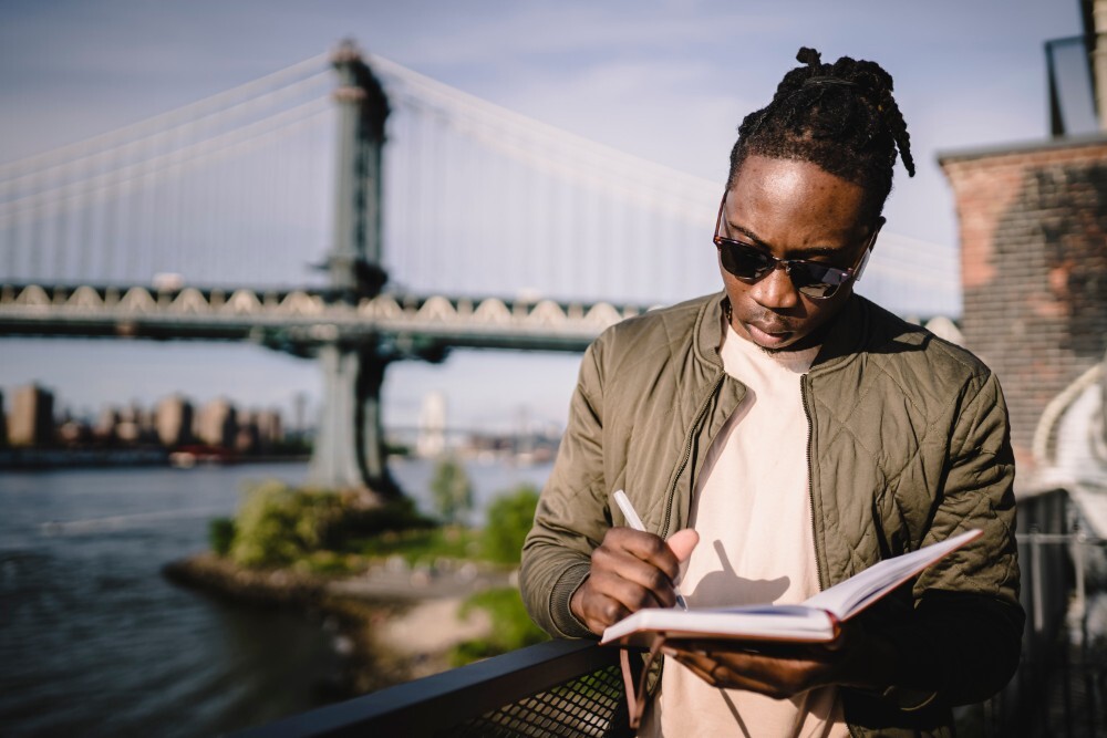 Man writes in planner in front of bridge