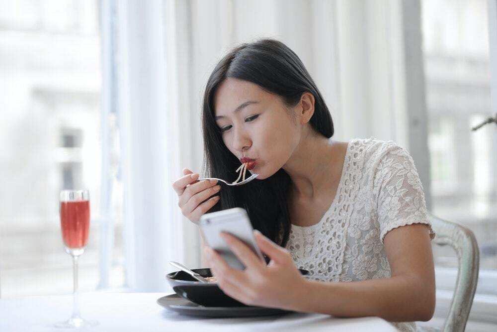 A woman eats noodles while looking at snackable content marketing.