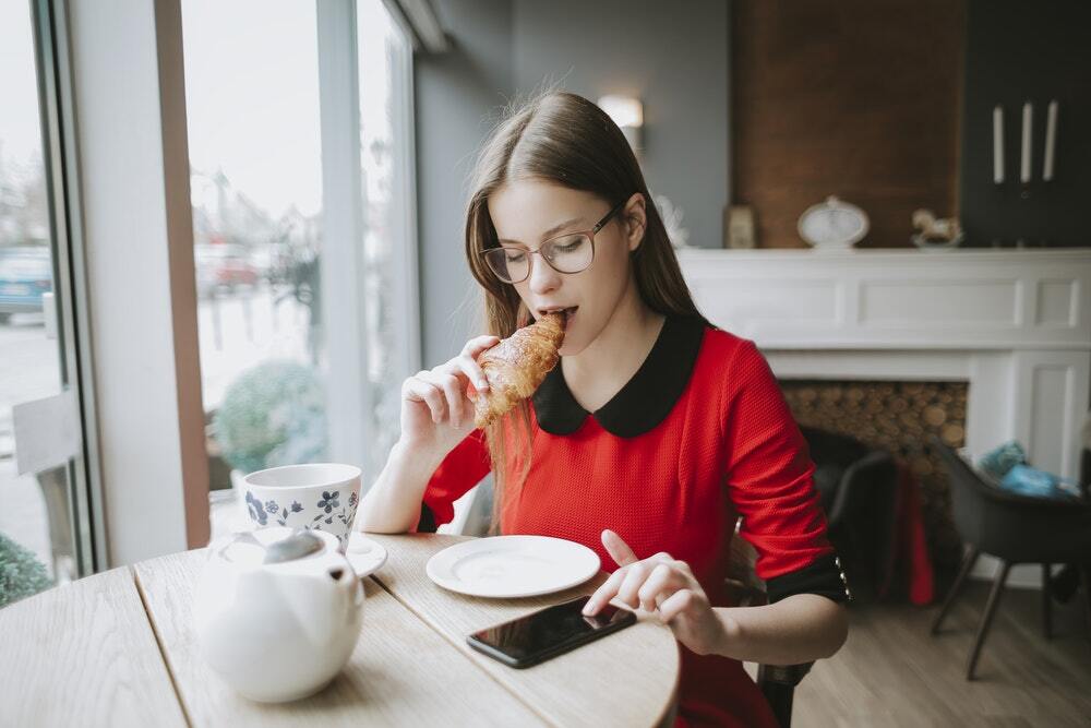 A woman wearing glasses eats a pastry while looking at snackable content marketing.