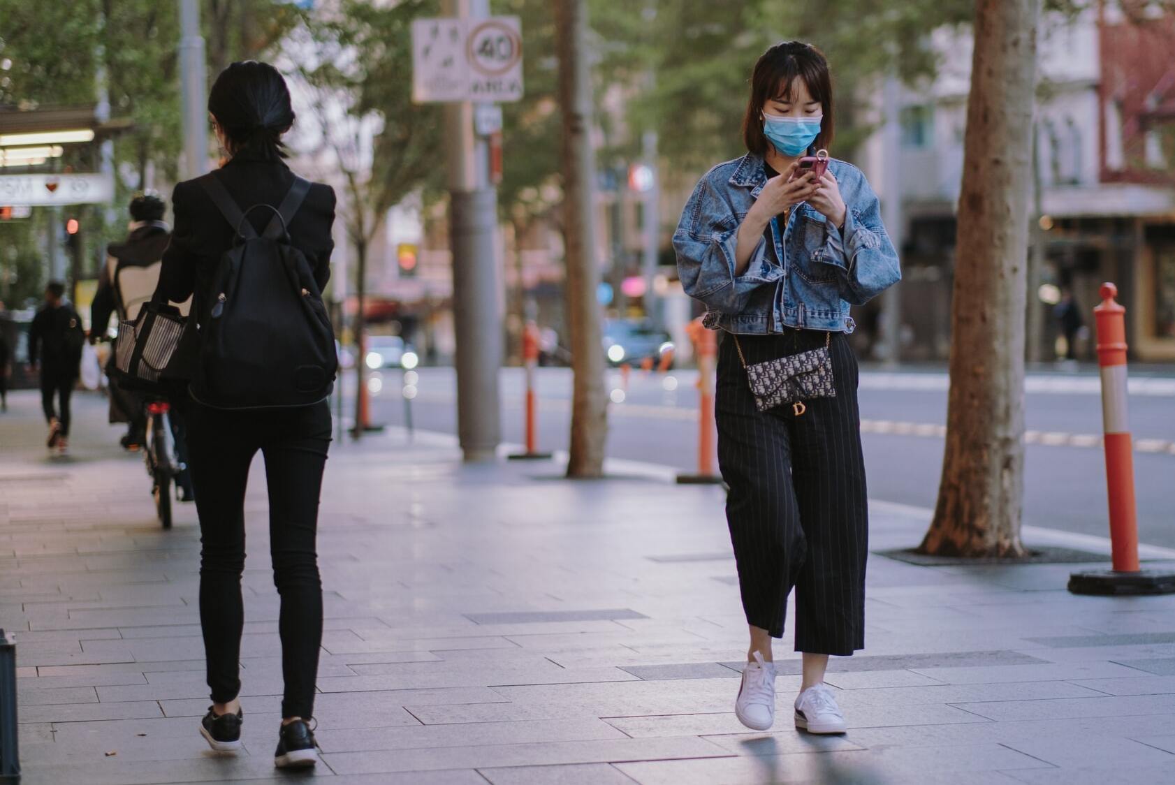 Woman in mask reads phone while practicing social distancing