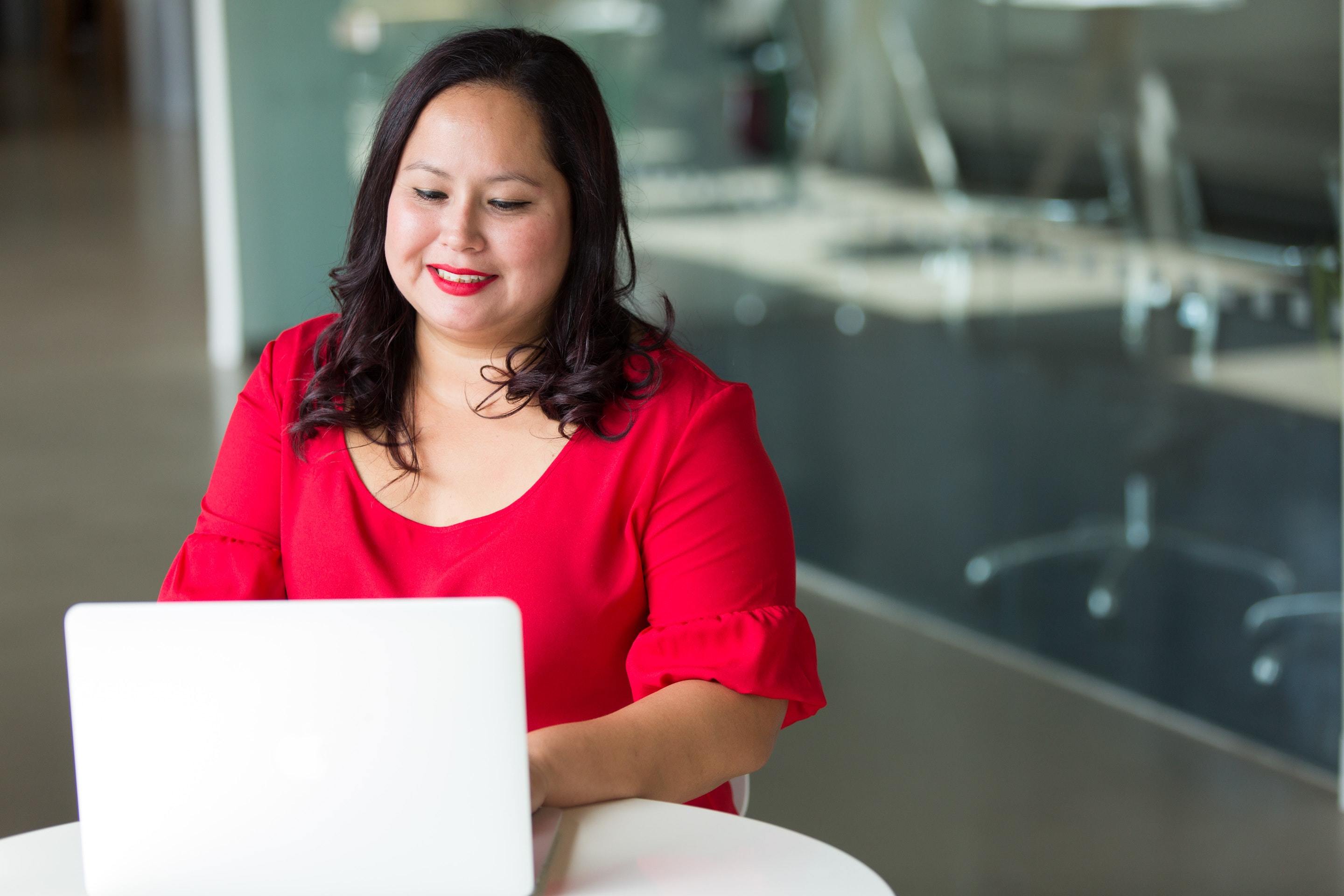 Woman in red top sitting behind laptop