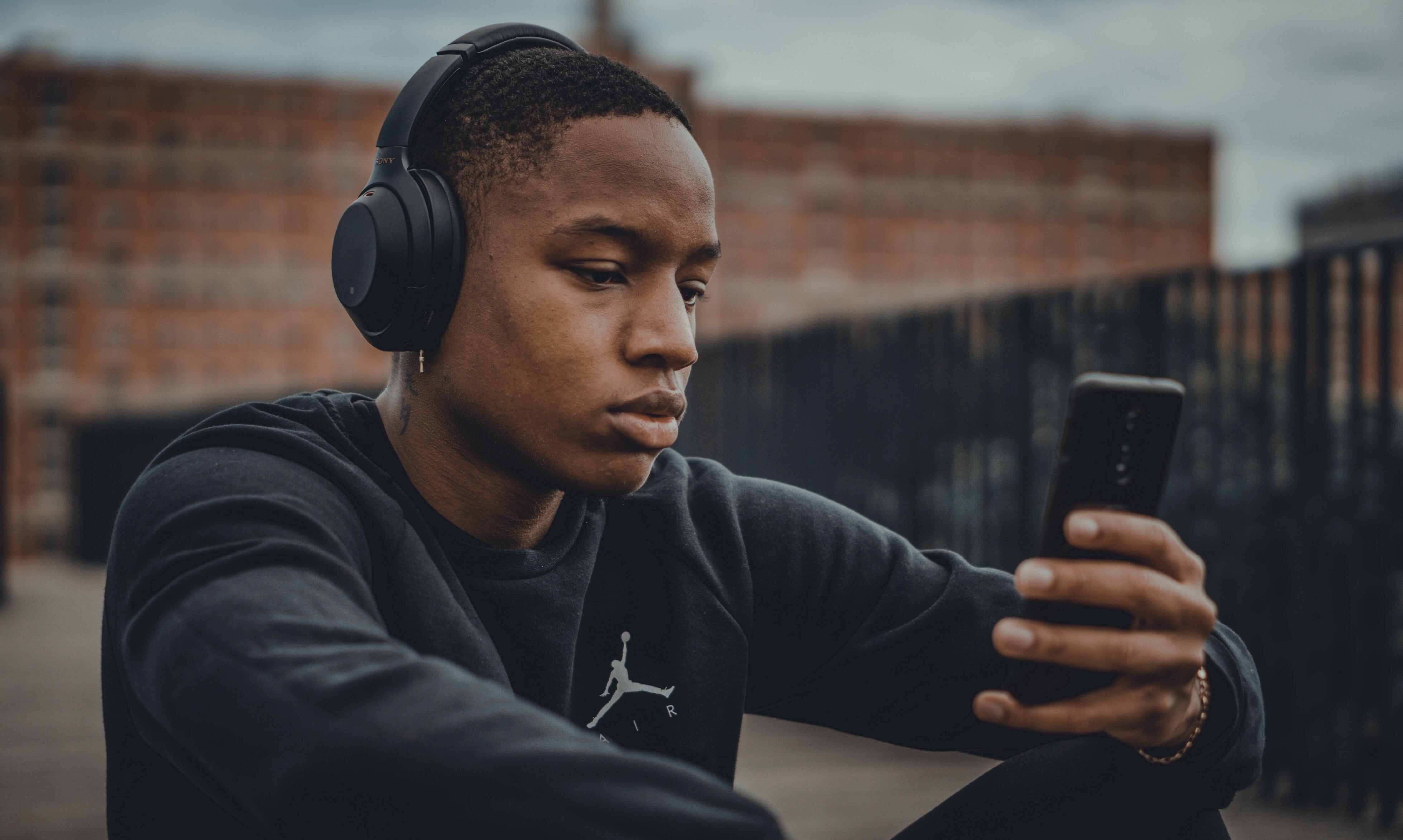 Man in black hoodie wearing headphones and holding a smartphone